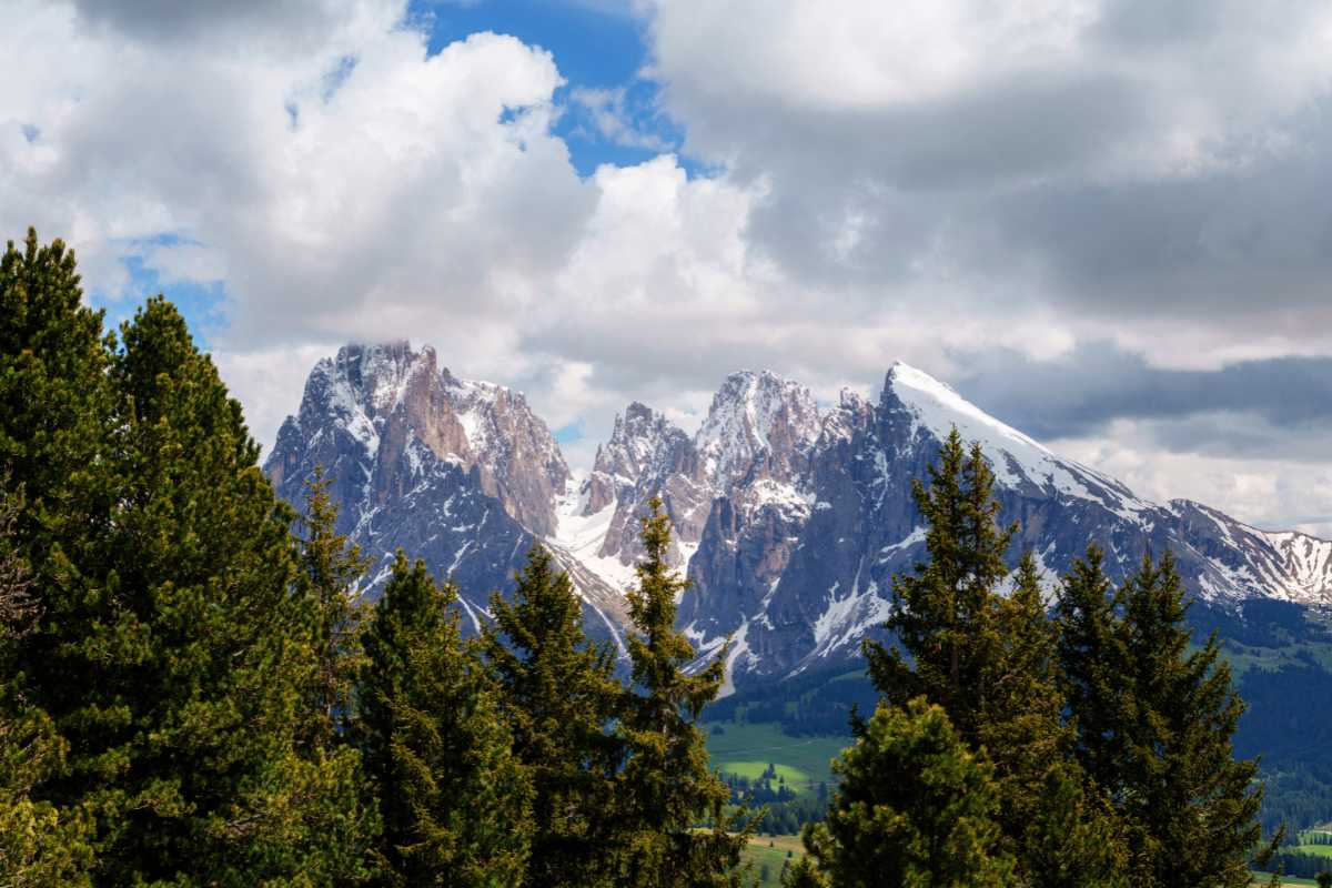 Vista panoramica dall’alto di Ortisei, con le Dolomiti sullo sfondo, accessi principali del paese visibili, auto in movimento sulle strade