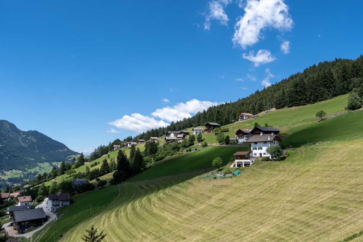 Scorcio panoramico del centro storico di Ortisei con le Dolomiti sullo sfondo, atmosfera mattutina, fiori ai balconi, passanti in abiti tipici